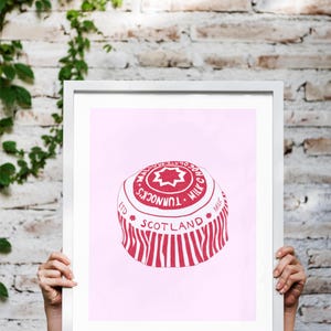 May include: A framed print featuring a red and white illustration of a Tunnock's Milk Chocolate wafer. The print includes the text "Tunnock's Milk Chocolate" and "Scotland" on a pink background.