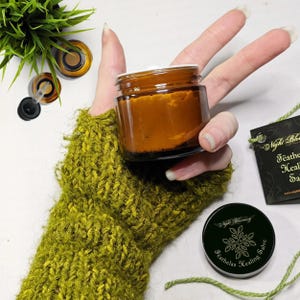 May include: A small amber glass jar with a white lid filled with a thick orange salve. The jar is labeled "Night Blooming Featherlas Healing Salve".