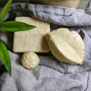 May include: Three bars of handmade soap, two rectangular and one shaped like a flower, on a grey fabric background.