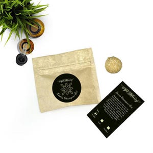 May include: A brown paper pouch with a black and white label that says "Lassea Shampoo Bar" and a small, round, light yellow shampoo bar.