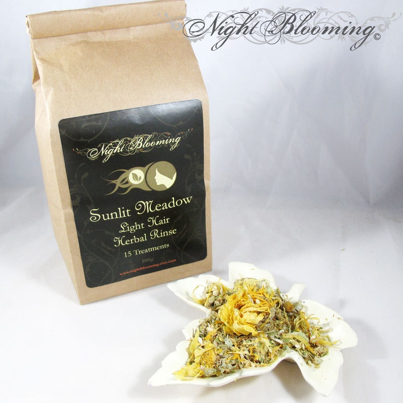 May include: A brown paper bag with a black label that reads "Night Blooming" and "Sunlit Meadow Light Hair Herbal Rinse 15 Treatments 100g". The bag is sitting on a white surface next to a white ceramic leaf-shaped dish filled with dried herbs.