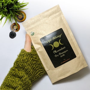 May include: A brown paper pouch with a black label that says "Moondust Dry Shampoo (Refill)" and a logo with three moons. The label also says "Night Blooming's" and includes a website address. The pouch is 75g.