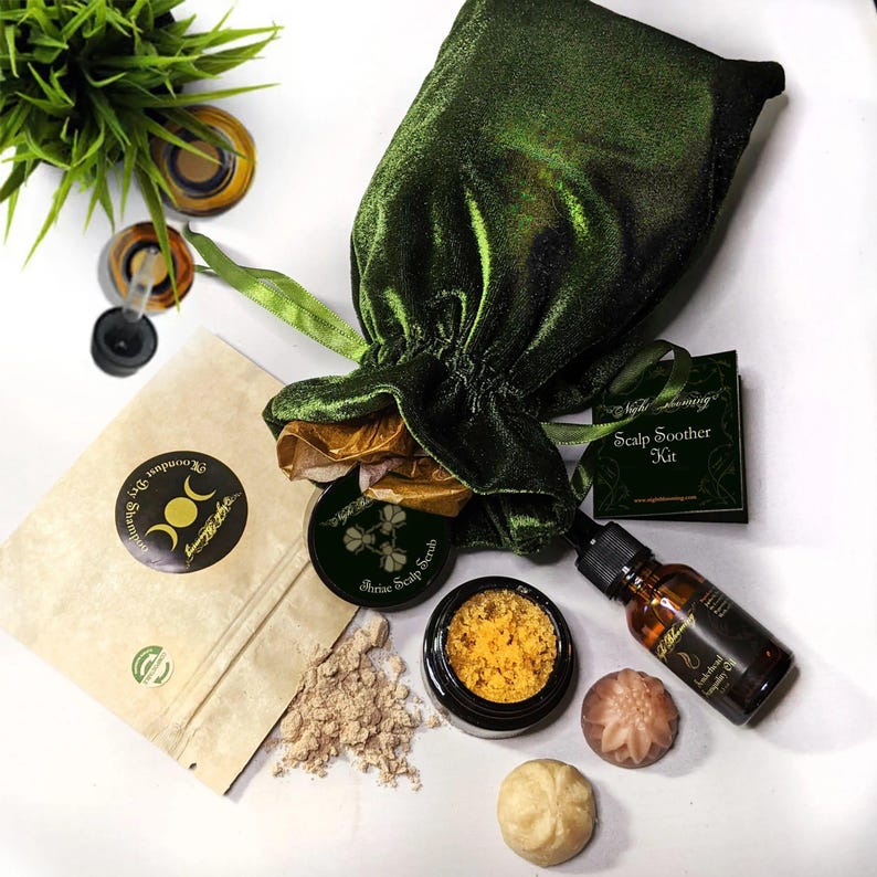 May include: A green velvet bag with a gold drawstring, a small brown paper bag with a label that says "Moonlit Shampoo", a small jar of yellow scrub with a label that says "Shrine Scalp Scrub", a small jar of brown powder, a small bottle of amber oil with a label that says "Scalp Oil", and two small round soaps. The label on the bag says "Scalp Soother Kit".
