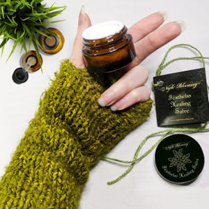 May include: A small amber glass jar with a white lid filled with a white salve. The jar is labeled "Night Blooming Featherlas Healing Salve" with the website address "www.nightblooming.com".