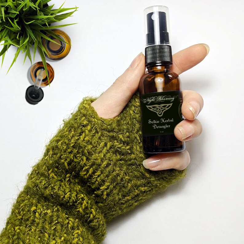 May include: A brown glass bottle with a black spray nozzle and a label that reads "Night Blooming Selkie Herbal Detangler 1 fl oz". The label has a gold Celtic knot design.
