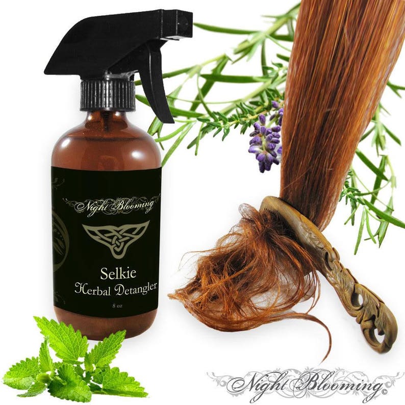 May include: A brown glass bottle with a black spray nozzle, labeled "Selkie Herbal Detangler" by "Night Blooming". The bottle is surrounded by sprigs of green herbs, including rosemary and lavender.