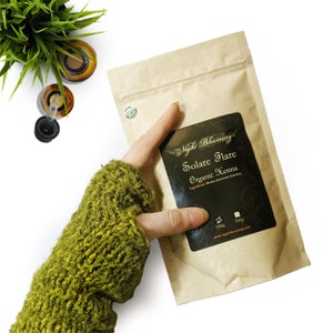 May include: A brown paper bag with a black label that says "Night Blooming" and "Solare Flare Organic Henna". The label also includes the ingredients "Henna (Lawsonia Inermis)" and the sizes "100g" and "500g". The bag is on a white surface.