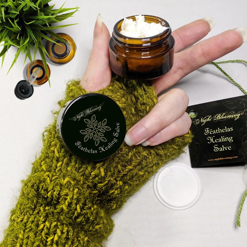 May include: A small amber glass jar with a white label that says "Night Blooming Feathalas Healing Salve" and a black label with the same text. The jar is open and contains a white salve. The jar is sitting on a green knitted glove.