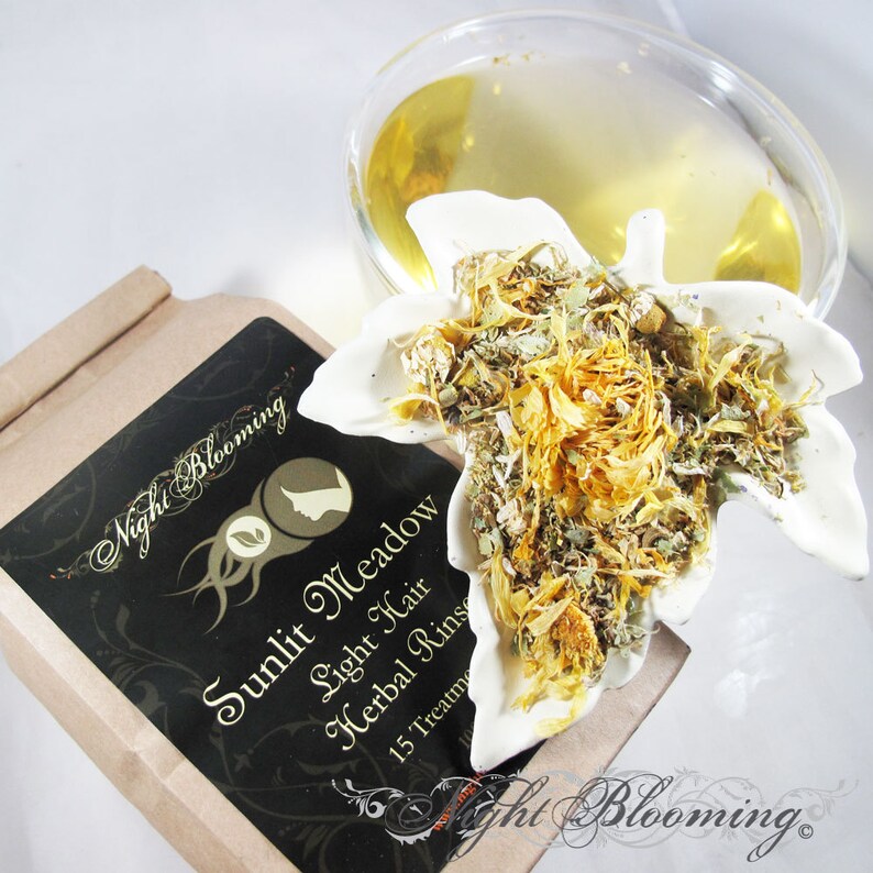 May include: A brown paper box with a black label that reads "Sunlit Meadow Light Hair Herbal Rinse 15 Treatments" and a white ceramic leaf-shaped dish filled with dried herbs and flowers.