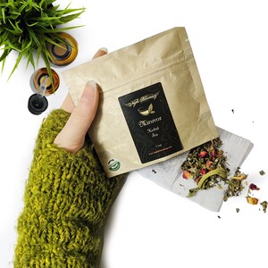 May include: A brown paper pouch with a black label that reads "Miruvor Herbal Tea 2 tsp www.nightblooming.com"  The pouch is open and a white tea bag with dried herbs and flowers is spilling out.