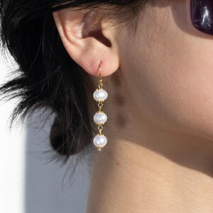 Peut inclure: Une paire de boucles d'oreilles en or avec trois perles blanches suspendues à une chaîne.