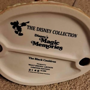 May include: A white ceramic base of a Disney figurine, featuring the text "THE DISNEY COLLECTION" and "Disney's Magic Memories." The base is marked "The Black Cauldron" and "LIMITED EDITION 2145/15,000."