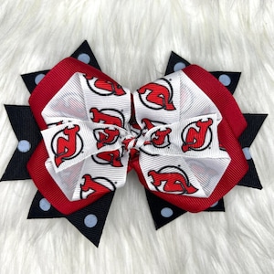 May include: A red and white hair bow with a black and white polka dot accent. The bow features a repeated pattern of a red hockey team logo.