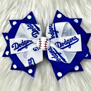 May include: A blue and white hair bow with white polka dots and a baseball in the center. The bow has the word "Dodgers" written on it.