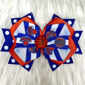 May include: Orange, blue, and white hair bow with a basketball and "Knicks" logo.