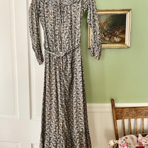 Peut inclure: Une robe vintage à motifs floraux noirs et beiges. La robe longue a des manches longues, un col montant et une ceinture à la taille. Elle est suspendue à une porte blanche, mettant en valeur sa coupe longue.