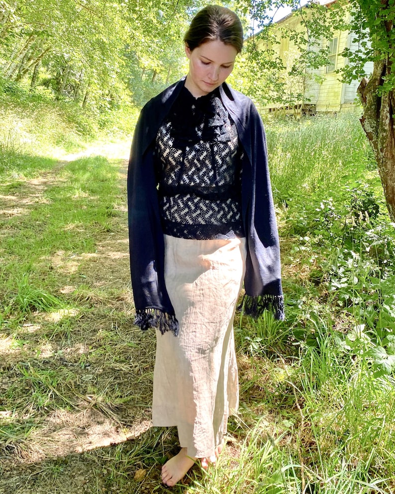 Puede incluir: Una mujer con un top estampado en blanco y negro, un chal azul marino con flecos y una falda beige. El atuendo se usa al aire libre en una zona herbosa con &aacute;rboles y un edificio al fondo.