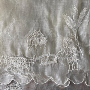 May include: White sheer fabric with embroidered designs of a house, a person, a palm tree, and an animal. The embroidery is done in white thread.