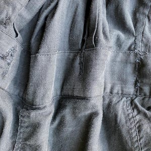May include: Close-up of the back of a black denim jacket with a zipper closure. The jacket has a textured, woven fabric and a slightly distressed look.