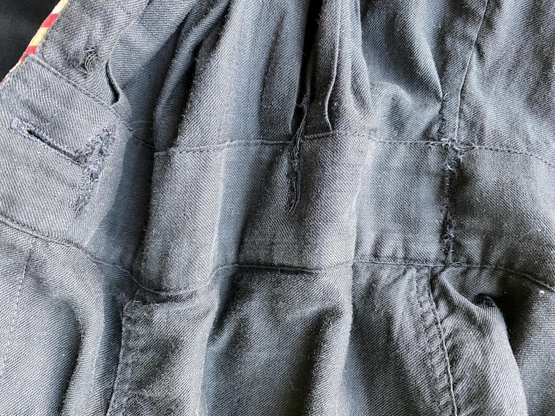 May include: Close-up of the back of a black denim jacket with a zipper closure. The jacket has a textured, woven fabric and a slightly distressed look.