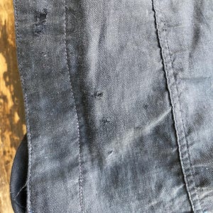 May include: Close-up of a dark gray denim jacket with a seam running down the side. The fabric has a subtle texture and there are a few small holes in the material.
