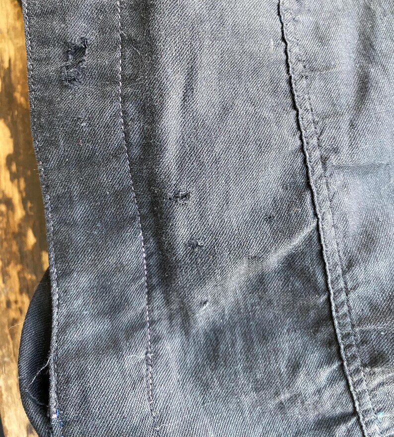 May include: Close-up of a dark gray denim jacket with a seam running down the side. The fabric has a subtle texture and there are a few small holes in the material.