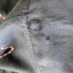 May include: Close-up of a dark blue fabric with a small hole and visible stitching.