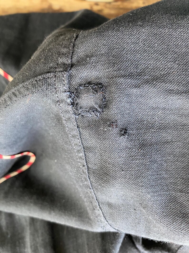May include: Close-up of a dark blue fabric with a small hole and visible stitching.