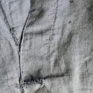 May include: Close-up of a dark gray fabric with a seam running down the center. The fabric has a textured weave and a small tear near the bottom.