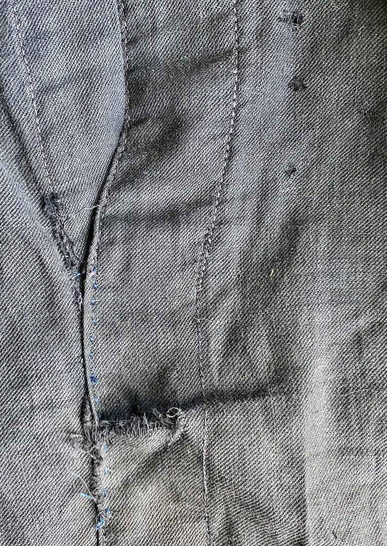 May include: Close-up of a dark gray fabric with a seam running down the center. The fabric has a textured weave and a small tear near the bottom.