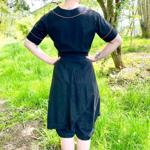 May include: A black linen dress with a short sleeve and a contrasting red stitching detail around the neckline and sleeves. The dress has a wrap style and a gathered skirt.