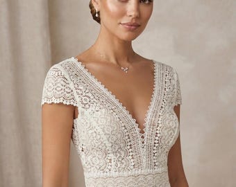 May include: An ivory-colored dress featuring a deep V-neckline and short cap sleeves. The bodice is crafted from intricate floral lace with scalloped edges along the neckline and waistline, transitioning into a smooth, solid-colored skirt.