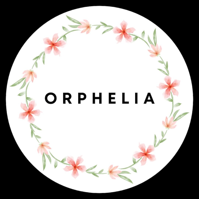 May include: A circular white sticker featuring the name ORPHELIA in bold black capital letters at the center. The text is surrounded by a delicate watercolor wreath composed of light pink five-petaled flowers and thin green leaves.