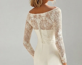 May include: A floor-length off-the-shoulder gown in ivory featuring long lace sleeves and a lace bodice overlay. The back of the garment displays a vertical row of small fabric-covered buttons extending from the neckline down to the waistline.