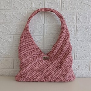 Pu&ograve; includere: Una borsa hobo all'uncinetto color rosa antico caratterizzata da una trama a coste diagonali su tutto il corpo. La borsa presenta un unico spallaccio integrato e una piccola etichetta metallica rettangolare centrata sulla parte anteriore.