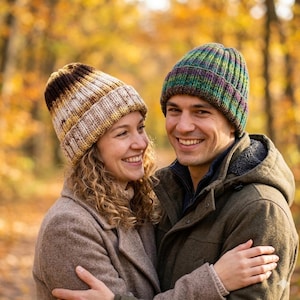 May include: Two knit beanies with ribbed textures. One beanie features a gradient of brown, cream, and tan tones. The other beanie displays a variegated pattern of green, purple, and blue hues. Both hats have a folded cuff design.