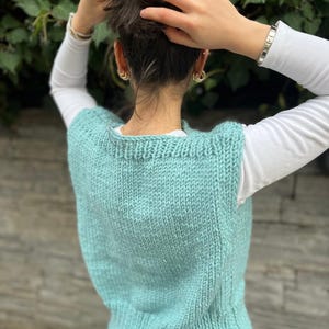 Op de afbeelding: Een tealblauwe gebreide vest zonder mouwen. De vest is gemaakt van een zacht, dik garen en heeft een eenvoudig, klassiek ontwerp.