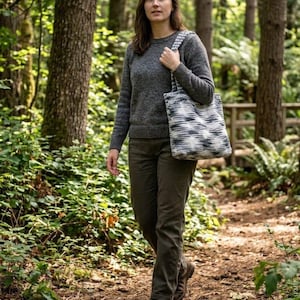 Könnte beinhalten: Ein anthrazitfarbener Pullover mit Rundhalsausschnitt, eine olivgrüne Hose und braune Leder-Wanderschuhe. Eine Umhängetasche mit schwarz-weißem, abstraktem Zickzackmuster wird über der Schulter getragen. Die Tasche hat eine rechteckige Form.