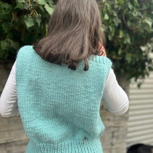 Op de afbeelding: Een tealblauwe gebreide vest met een geribbelde onderkant. De vest is mouwloos en heeft een V-hals.