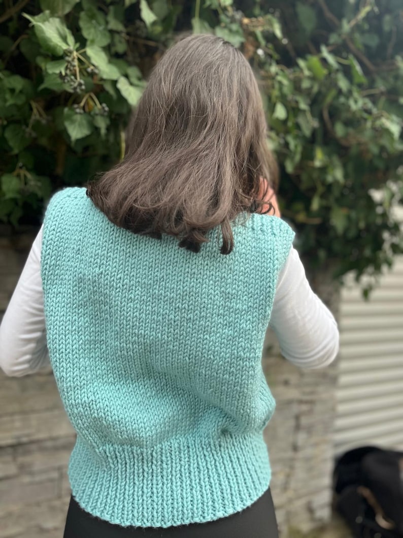 Op de afbeelding: Een tealblauwe gebreide vest met een geribbelde onderkant. De vest is mouwloos en heeft een V-hals.