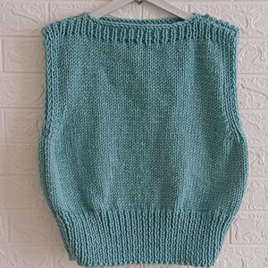 Op de afbeelding: Een gebreid vest zonder mouwen in een lichtblauwe kleur. Het vest heeft een eenvoudig ontwerp met een ronde hals en een geribbelde zoom.