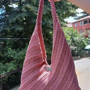 Pu&ograve; includere: Una borsa hobo all'uncinetto color rosa polvere con un motivo a coste diagonali e una tracolla integrata. Una piccola etichetta rettangolare in metallo color argento &egrave; fissata al centro sul davanti con il testo inciso "Handmade".