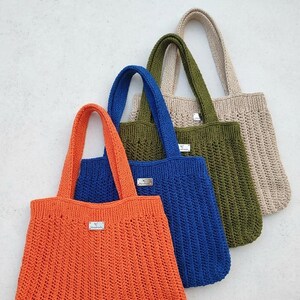 May include: A set of four crochet tote bags in orange, blue, olive green, and beige. Each bag features a vertical ribbed stitch pattern, two sturdy handles, and a small rectangular silver-toned metal tag attached to the front center.