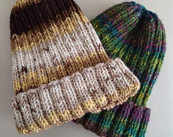 May include: Two knit beanies with folded cuffs. One beanie features a variegated yarn pattern in shades of dark brown, tan, and cream. The second beanie is crafted from a multi-colored yarn blend displaying vibrant hues of green, blue, and purple.