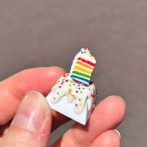 May include: A small white cake with rainbow frosting and sprinkles. The cake is topped with a rainbow-colored layer cake.