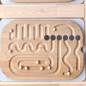 May include: Two wooden boards with carved tracks and holes for marbles. The top board has a rainbow-shaped track with 10 holes at the top and 10 holes at the bottom. The bottom board has a maze-like track with 6 holes at the top and 6 holes at the bottom.