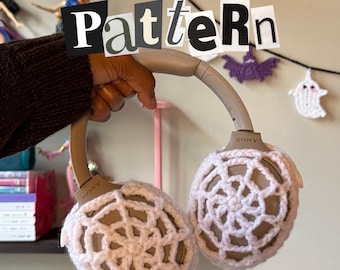 May include: A pair of Sony headphones with light pink crocheted ear covers. The text "Pdf Pattern" is displayed at the top, and "By: Stitched by Soleil" is at the bottom. Decorative Halloween-themed crochet pieces are in the background.