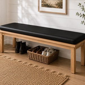 May include: A rectangular wooden bench featuring a smooth, light-toned natural wood frame and a long, flat black upholstered seat cushion. The bench is supported by four sturdy legs and includes a woven wicker basket underneath for storage.