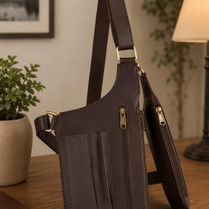 May include: A dark brown leather crossbody bag featuring an adjustable strap with brass-toned hardware, multiple exterior vertical zippered pockets, and integrated card slots on the front panel for organized storage.