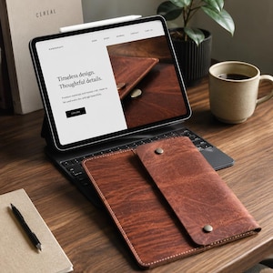 May include: A brown leather tablet sleeve with a fold-over flap and two metal snap buttons. The sleeve is placed in front of a tablet displaying a website with the text Timeless design. Thoughtful details. and a white stylus on top.